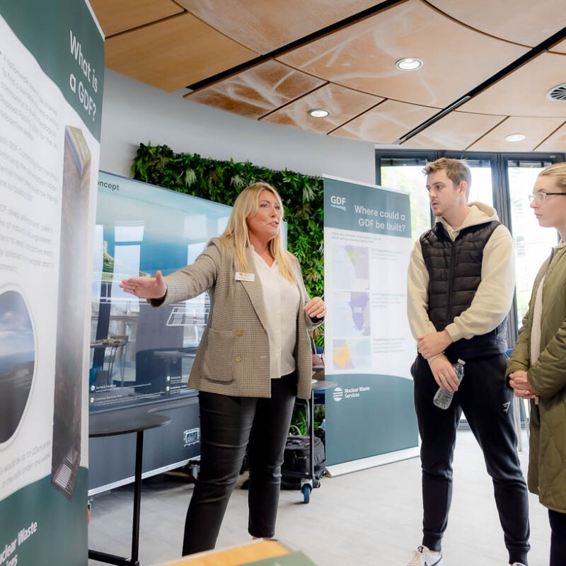 Lady talking to two people standing in front of NWS banners at an event