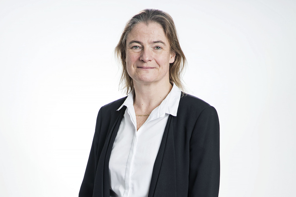 A Woman staring into camera while wearing a white shirt and black blazer.