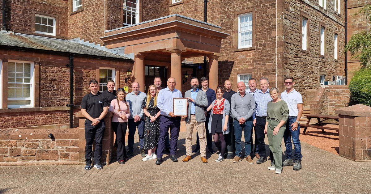 A group of colleagues, on a sunny day, holding an award for safety outside of an office.