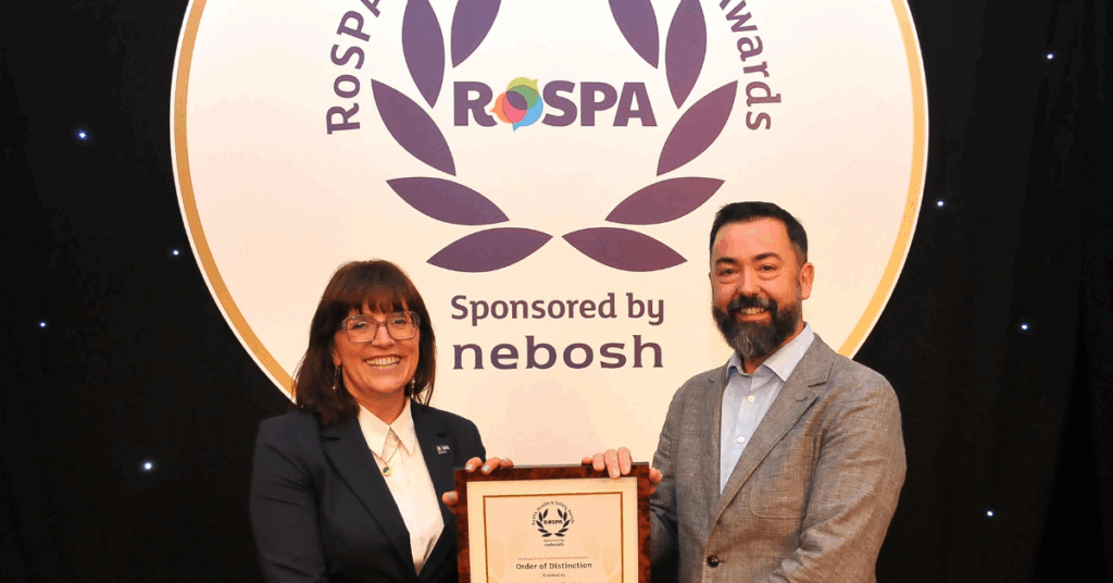 A male employee receiving a framed award from a woman, they are in front of a branded backdrop