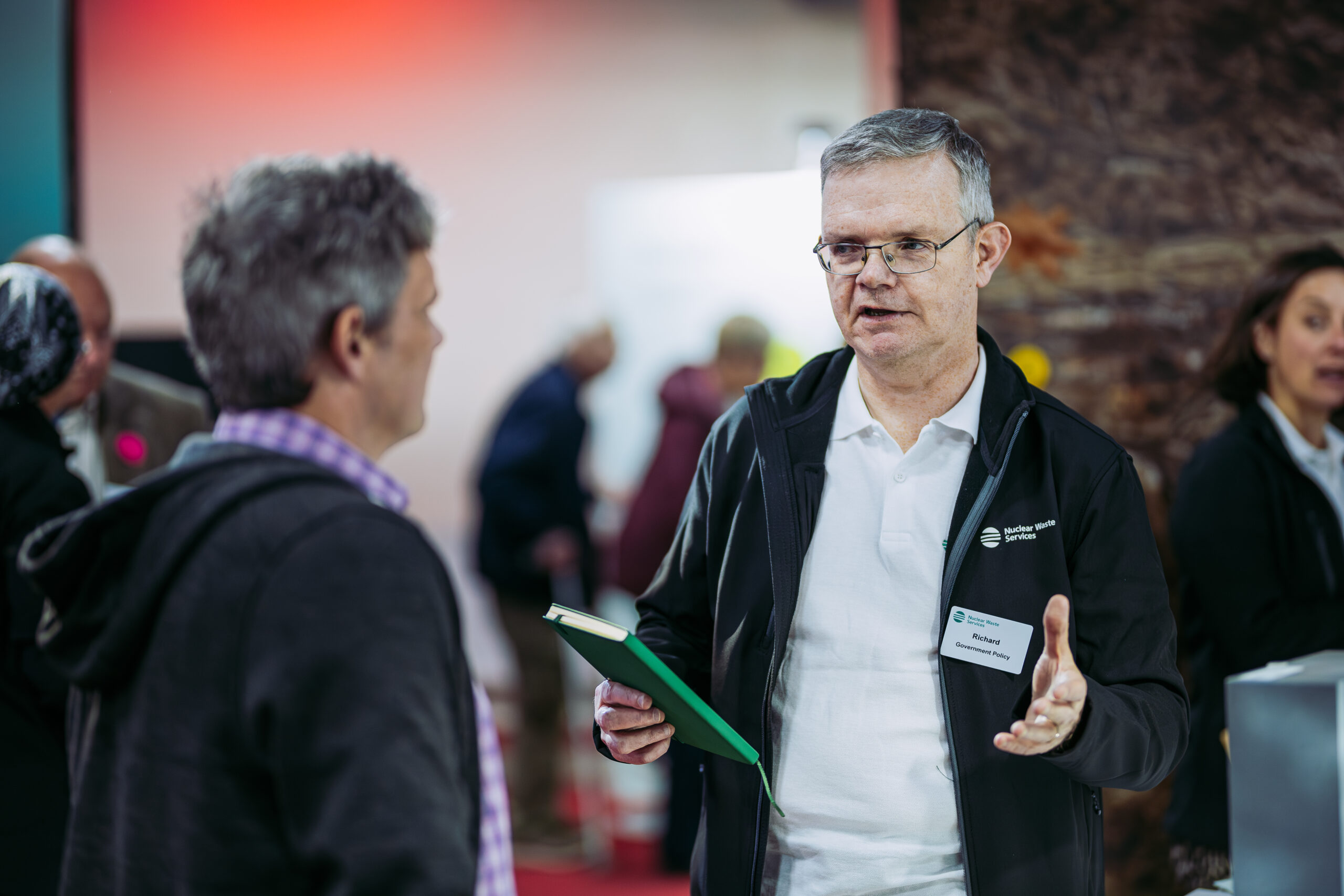 Man holding notebook talking to another man at an event