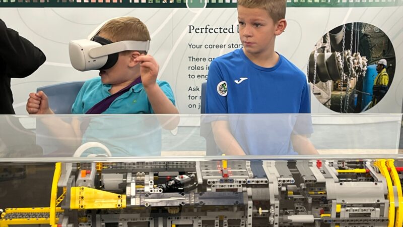 Two young boys stood next to a Lego model of a borehole drilling machine. One boy is wearing a VR headset.