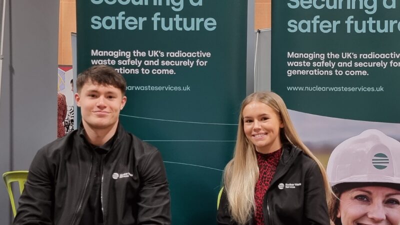Two young apprentices sitting in front of 2 pull-up banners at an event