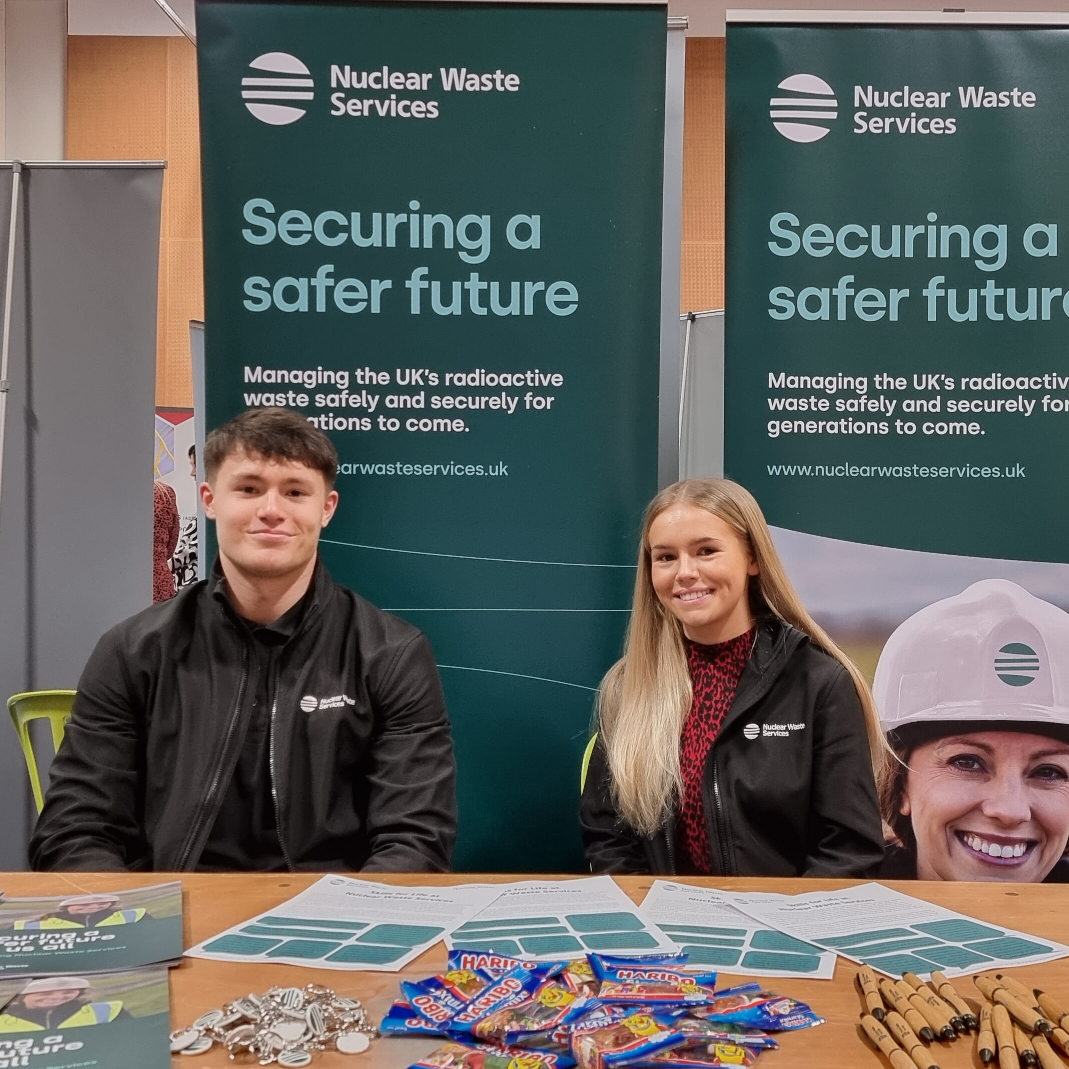 Two young apprentices sitting in front of 2 pull-up banners at an event