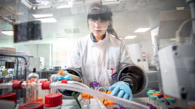 A person in a laboratory wearing personal protective equipment and testing samples