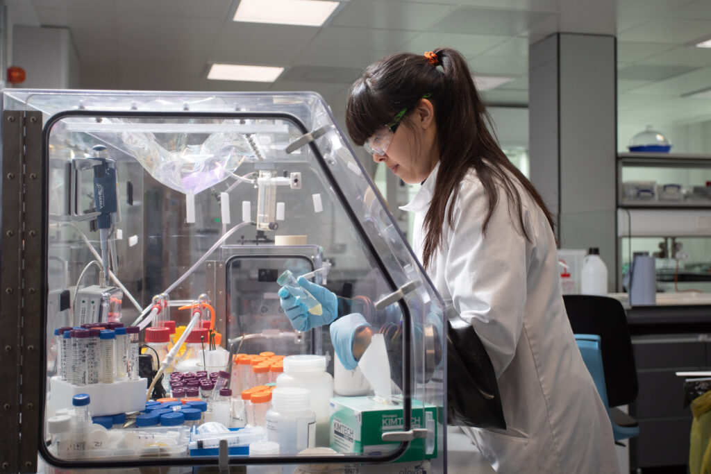 A person in a laboratory wearing personal protective equipment and testing samples